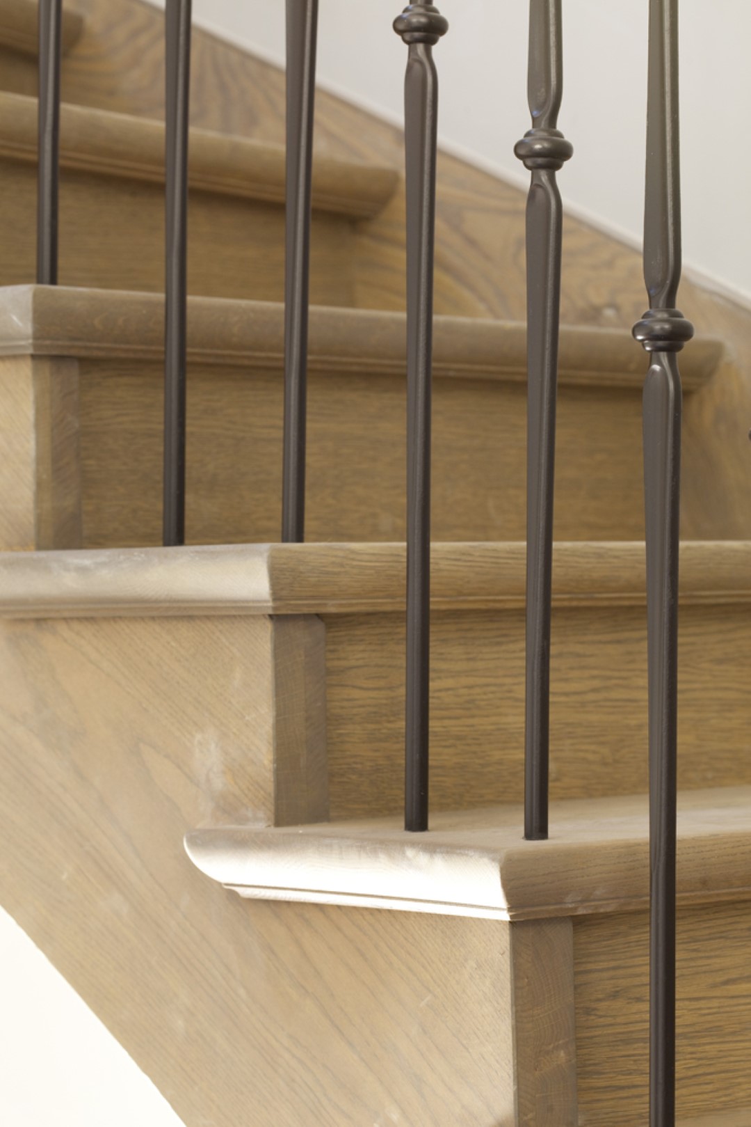 Close-up van een houten trap met afgeronde treden en zwart metalen spijlen met sierlijke details.
