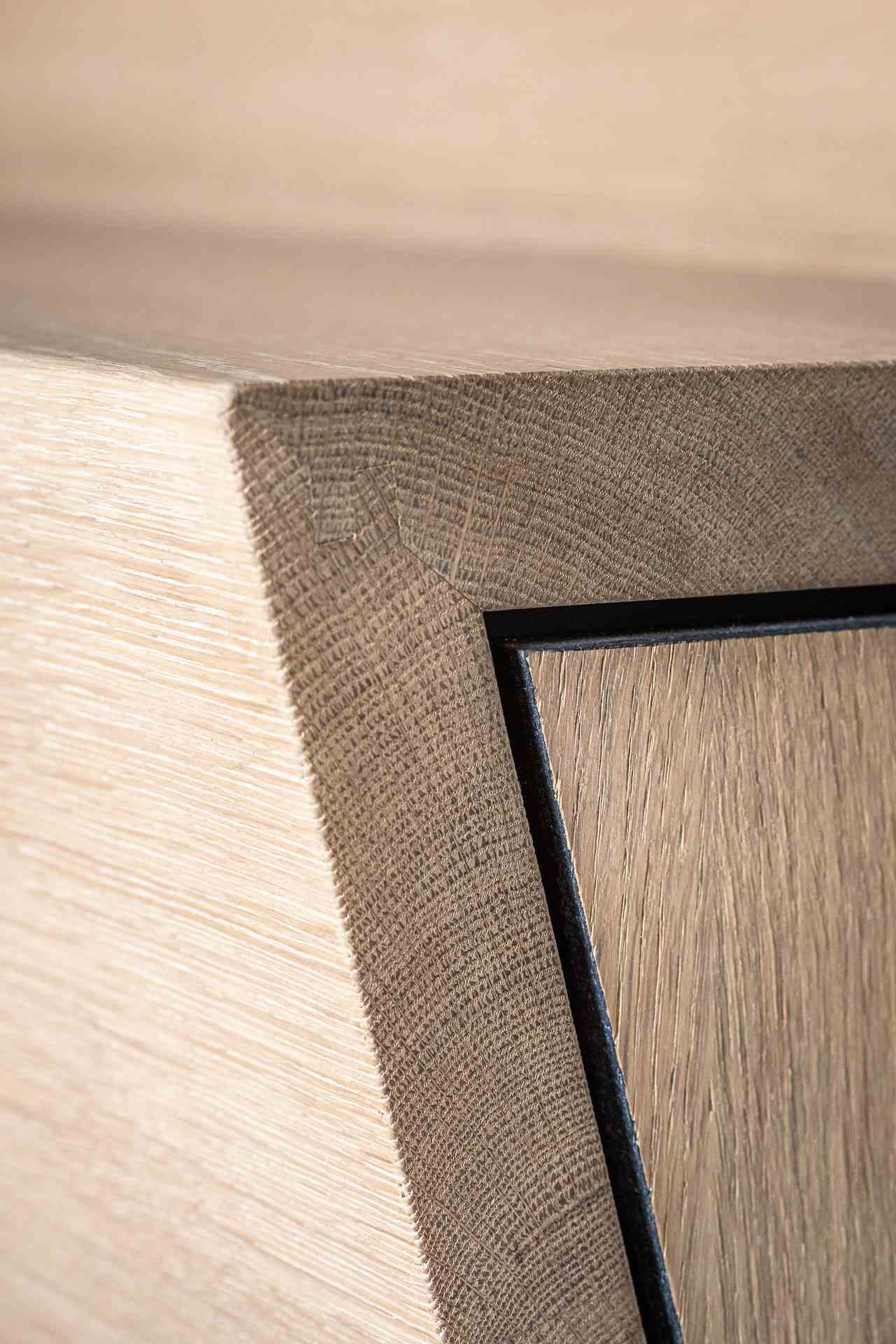 Close-up van de strakke hoekafwerking van een moderne houten trap met fijne houtnerf en zwarte belijning.