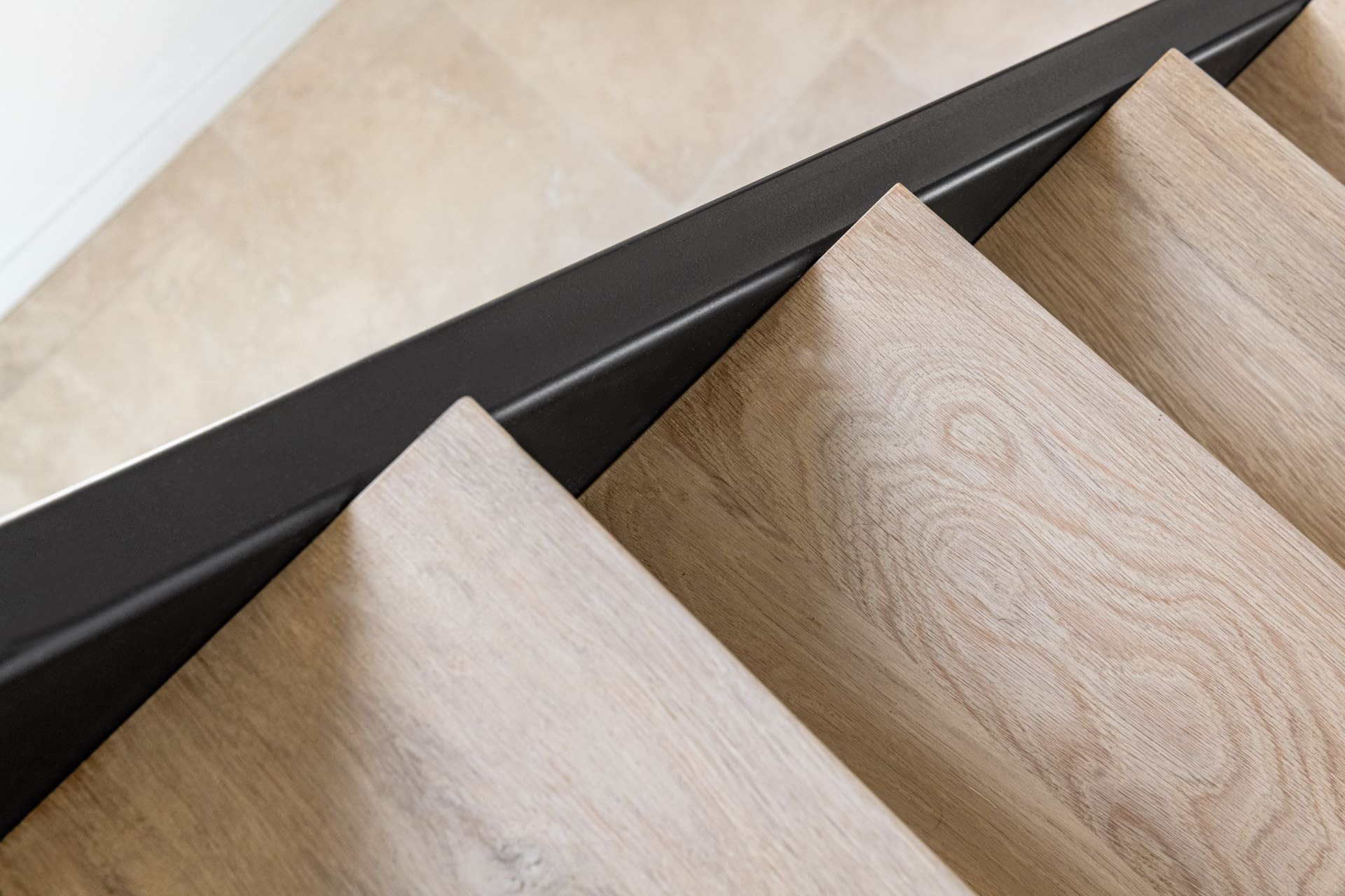 Close-up van lichte houten traptreden met een strakke zwarte stalen zijkant in een modern interieur.