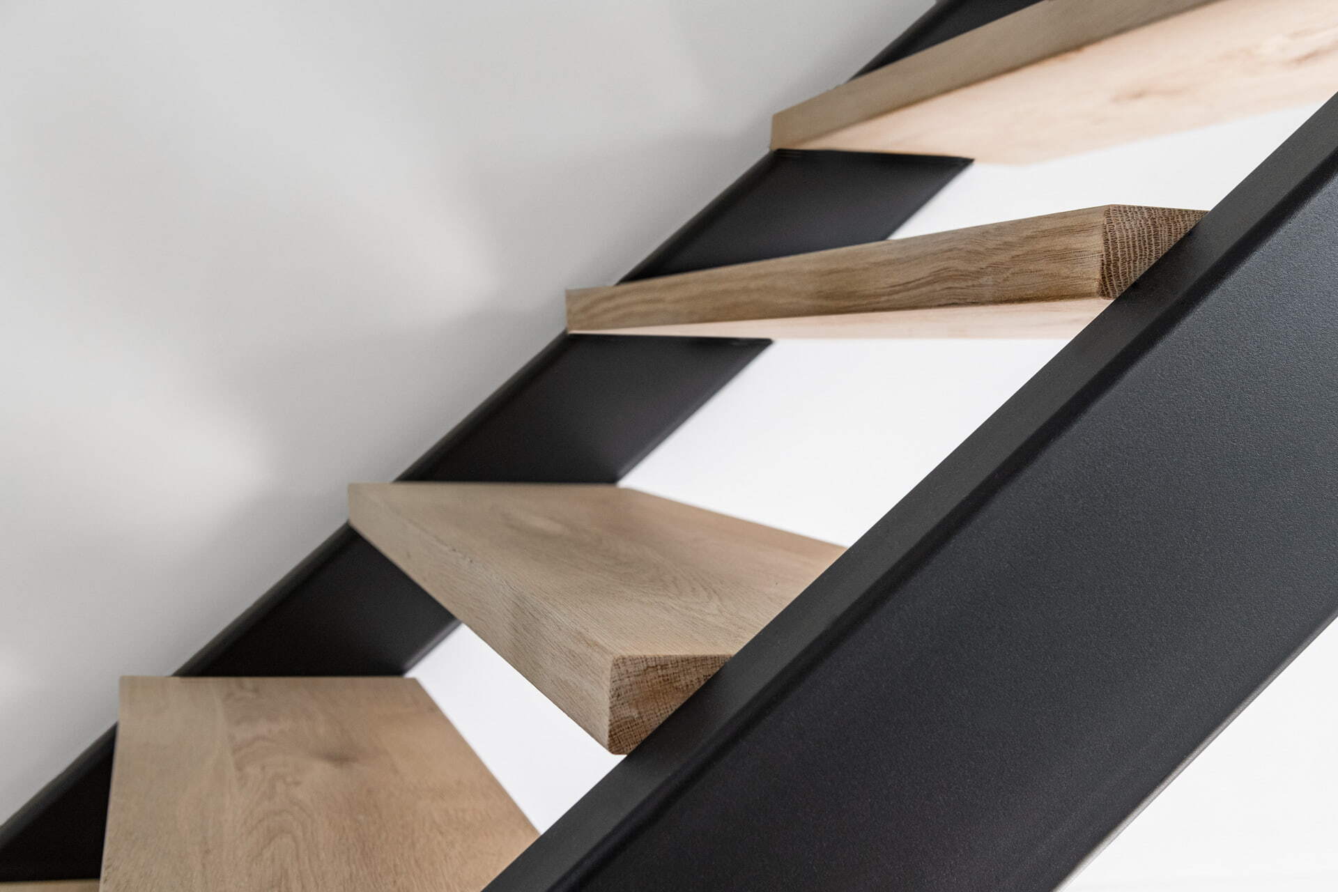 Close-up van zwevende houten traptreden met een zwarte metalen zijkant tegen een witte muur in een modern interieur.