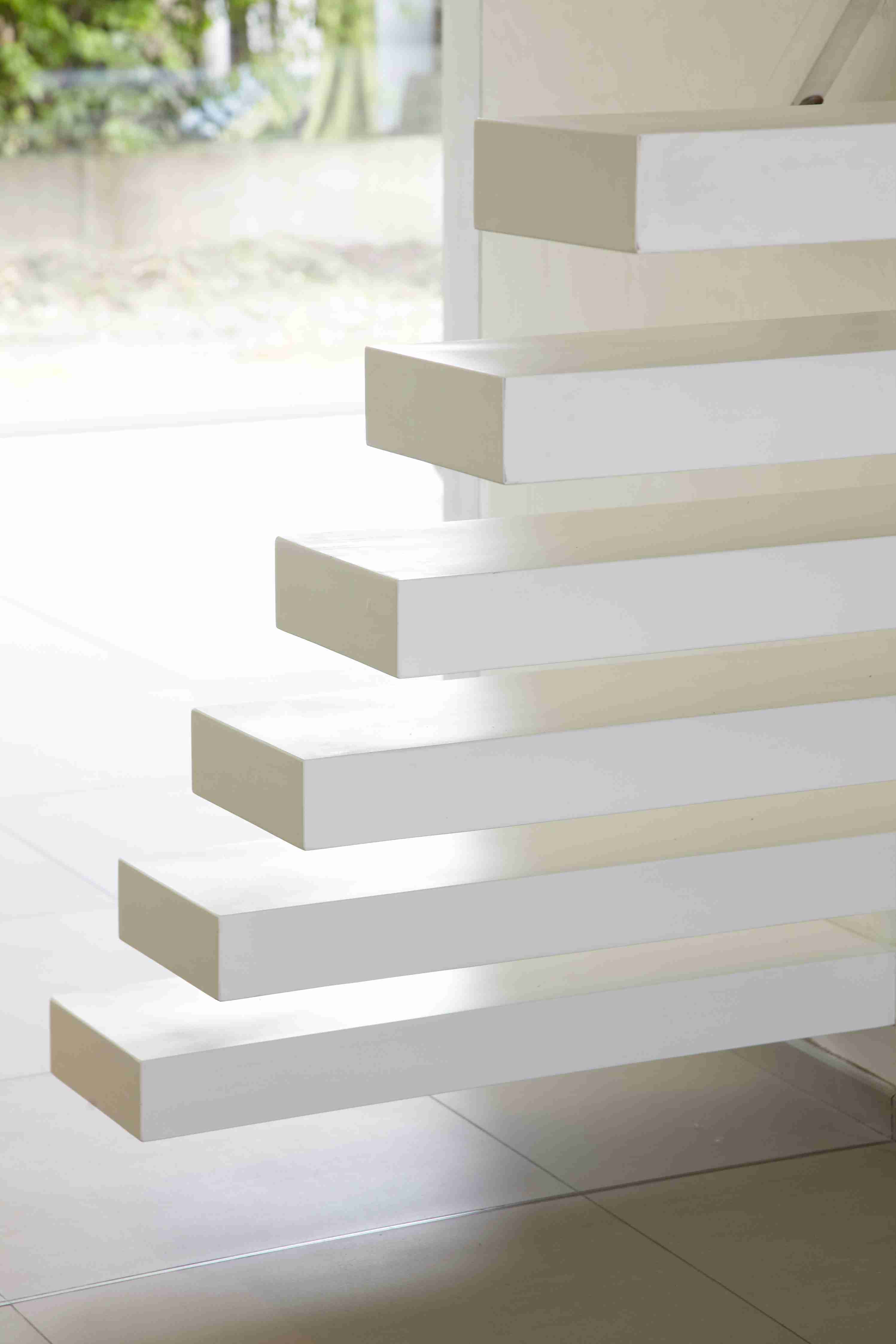 Close-up van minimalistische zwevende traptreden in wit, met scherpe lijnen en schaduweffecten op een lichtgrijze tegelvloer.