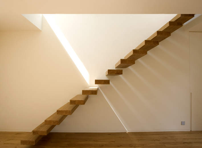Architectonisch opvallende dubbele zwevende trap met houten treden die elkaar in het midden raken, met dramatisch lichtinval dat scherpe schaduwen werpt op de witte muur.