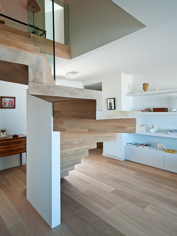 houten trap met zwevende treden en witte zijstructuur in een open, licht interieur met houten vloer, witte wandkasten en decoratieve elementen.