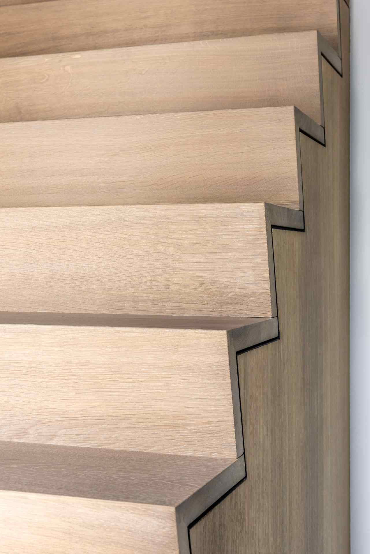 Minimalistische trap met open houten treden en een strak zwart stalen frame in een licht en modern interieur.