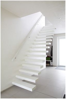 Minimalistische witte trap met zwevende treden en witte leuning in een strak afgewerkte ruimte met lichtgrijze vloer en veel natuurlijk licht.